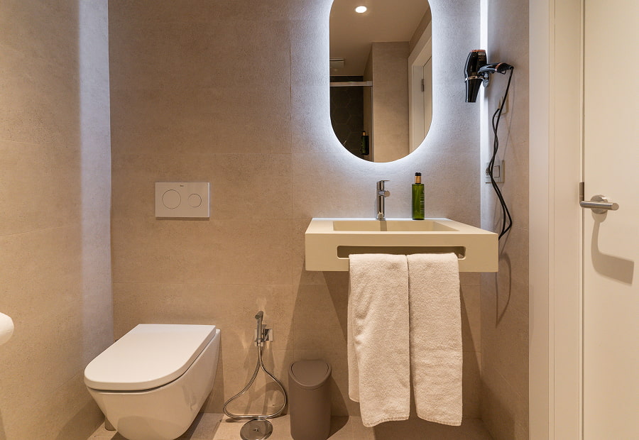 Bathroom with washbasin and backlit mirror Bathroom with sink, backlit mirror, towels, amenities and hairdryer